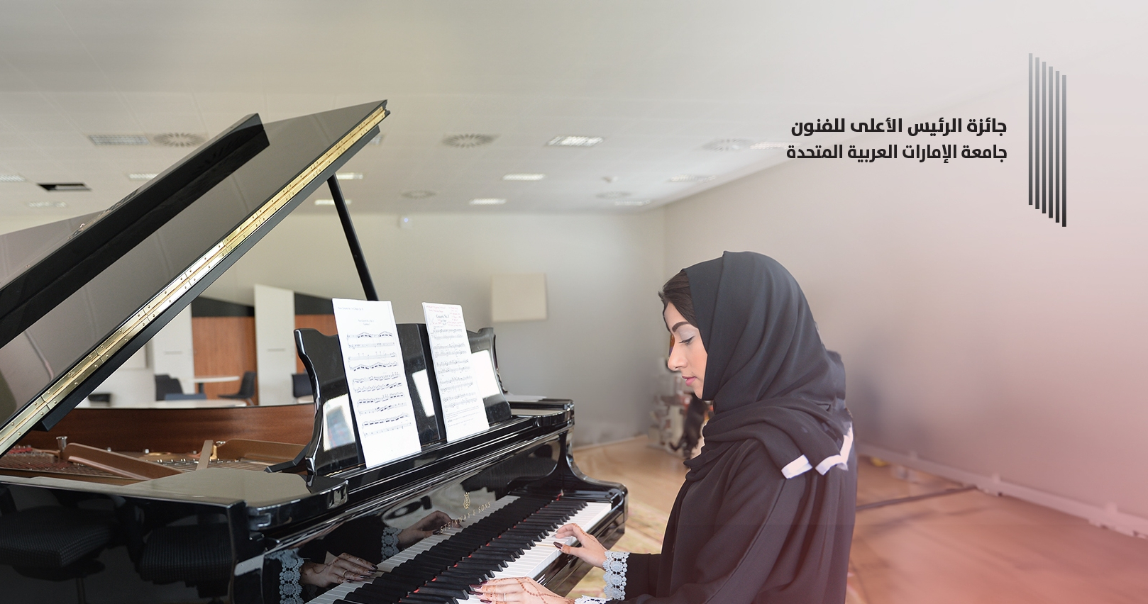 امرأة شابة ترتدي حجابًا أسود تعزف على بيانو كبير في غرفة موسيقى مضيئة، تمثل جائزة المستشار للفنون في جامعة الإمارات العربية المتحدة.