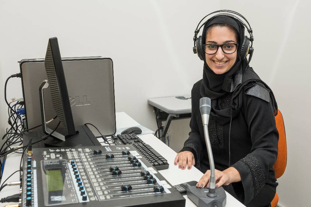 A female student wearing headphones and working at a professional audio mixing console.