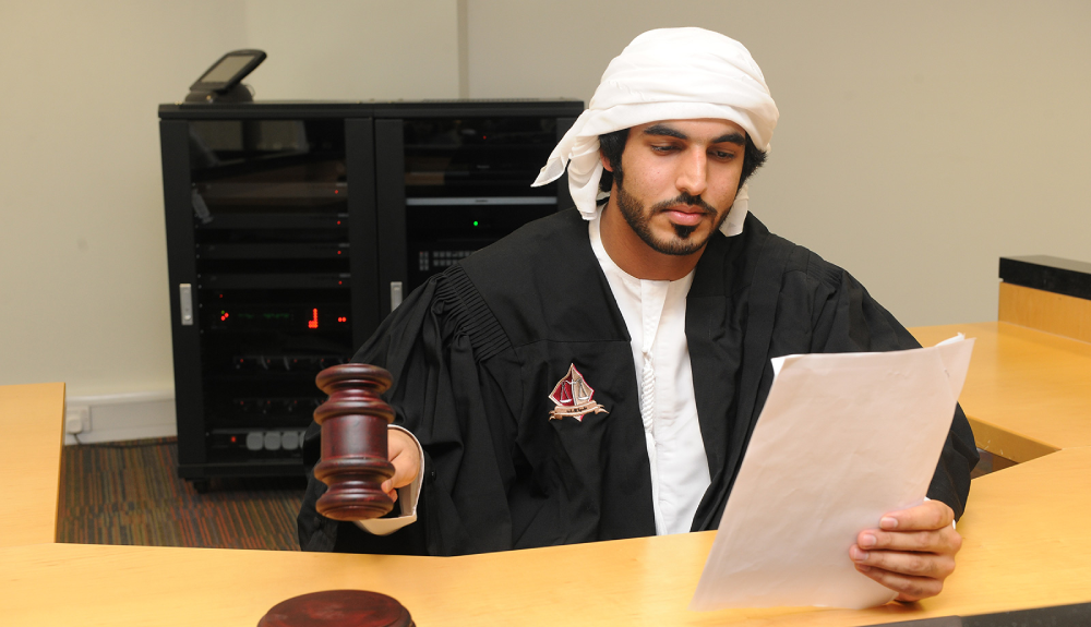 A College of Law student in a judicial robe holding a gavel while reading a legal document.