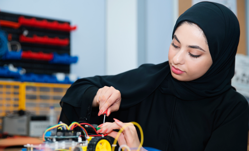 امرأة ترتدي حجابًا أسود تعمل على أسلاك ومكوّنات إلكترونية على لوحة دارة في مختبر تكنولوجي في مركز الذكاء الاصطناعي والابتكار الرقمي (AIDI) في جامعة الإمارات العربية المتحدة.