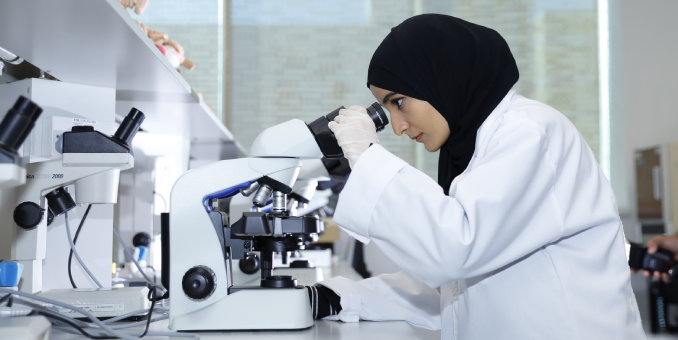 The UAEU Crescent building at United Arab Emirates University with clear blue skies, lush greenery, and the UAE flag visible on both sides of the structure.